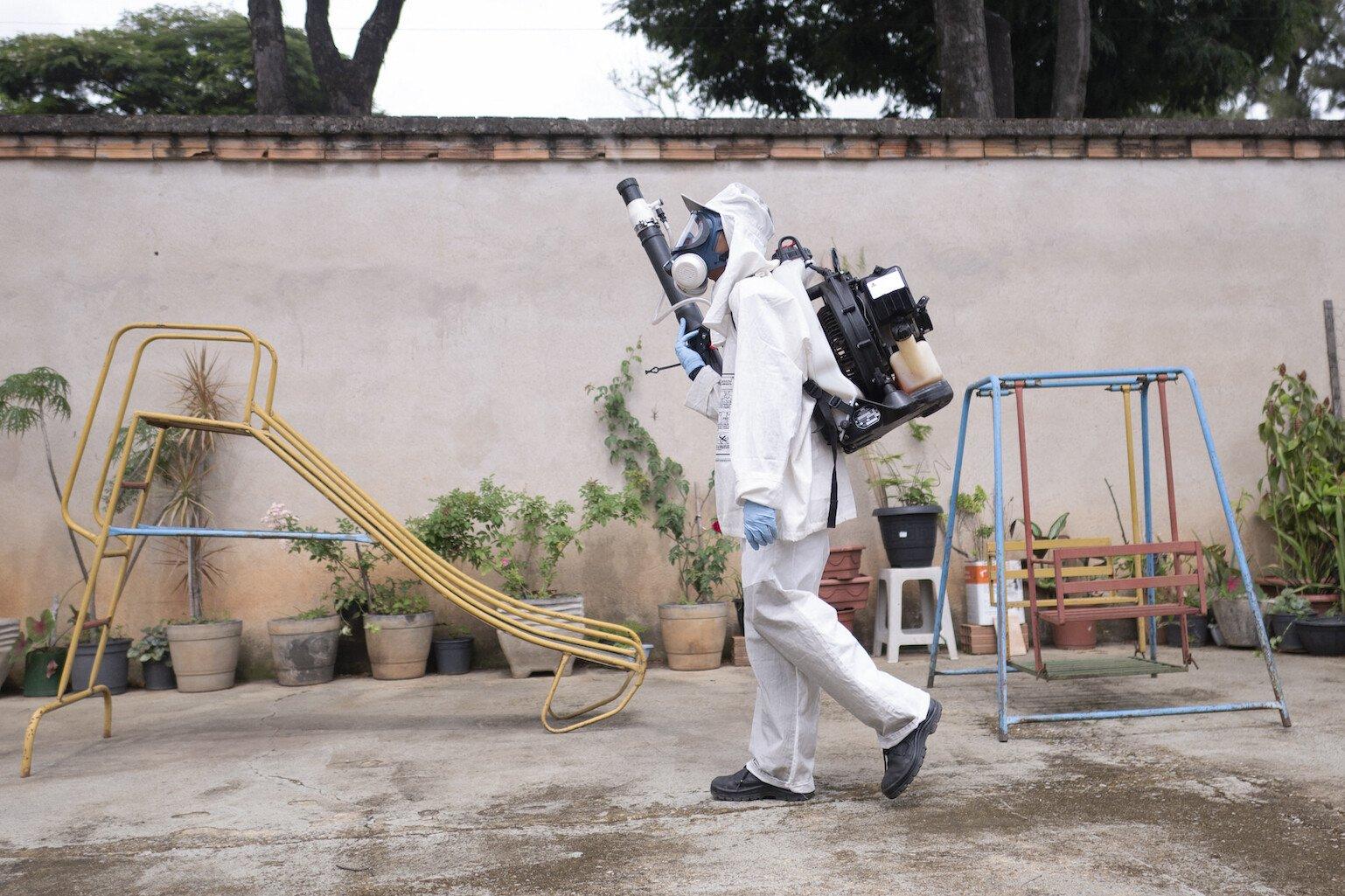 A person in a white hazmat suit holding a fumigation machine.