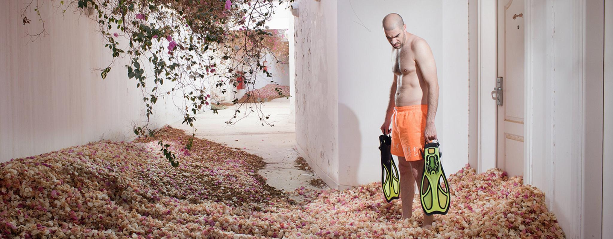 A man holding two flippers stands in a hotel room overgrown with rose bushes