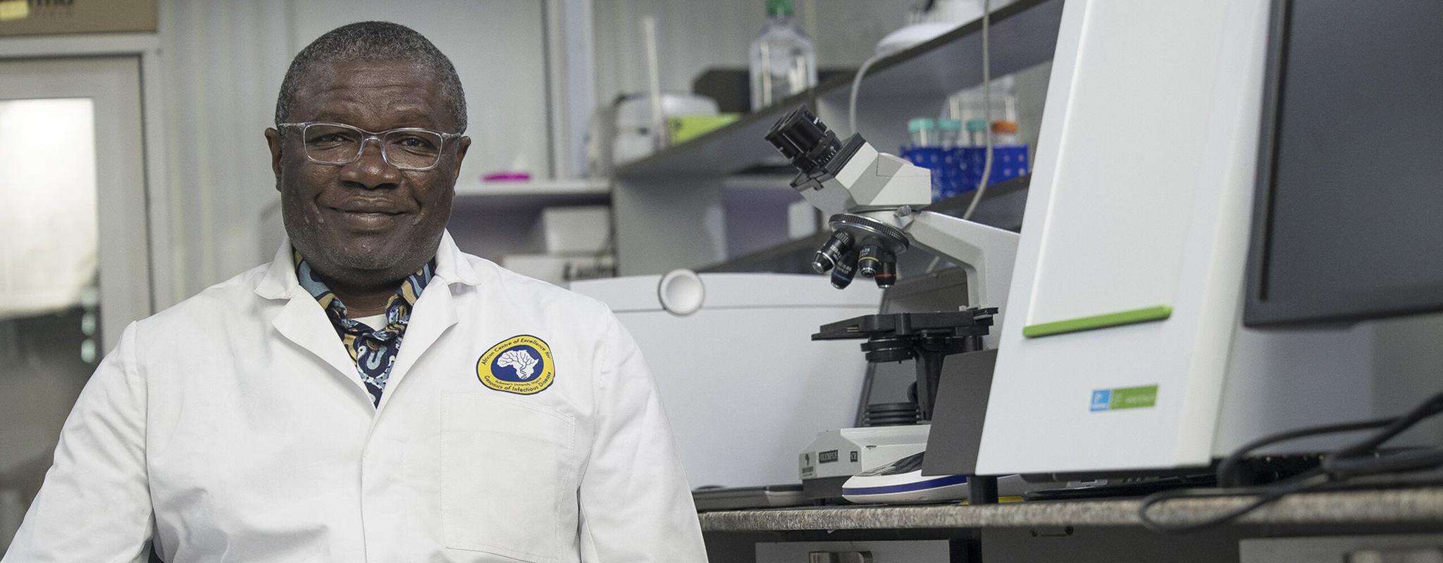 Dr Christian Happi is sat in his lab, wearing a labcoat and surrounded by equipment.