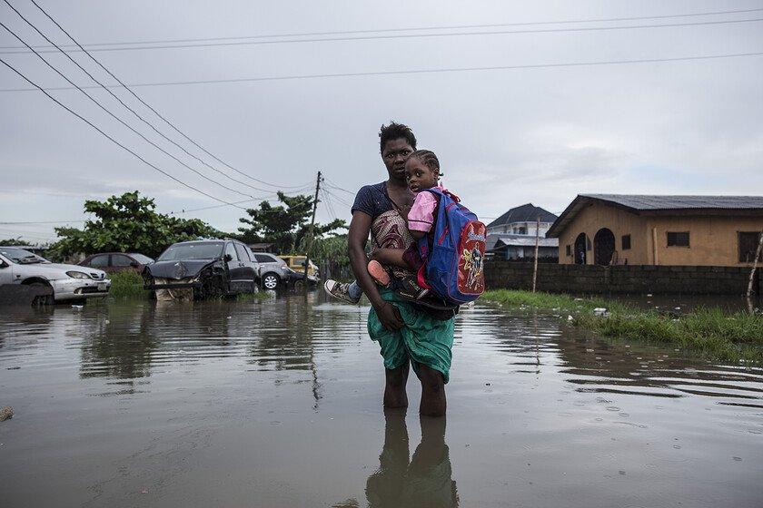 A mother carries her children to school through a flooded street