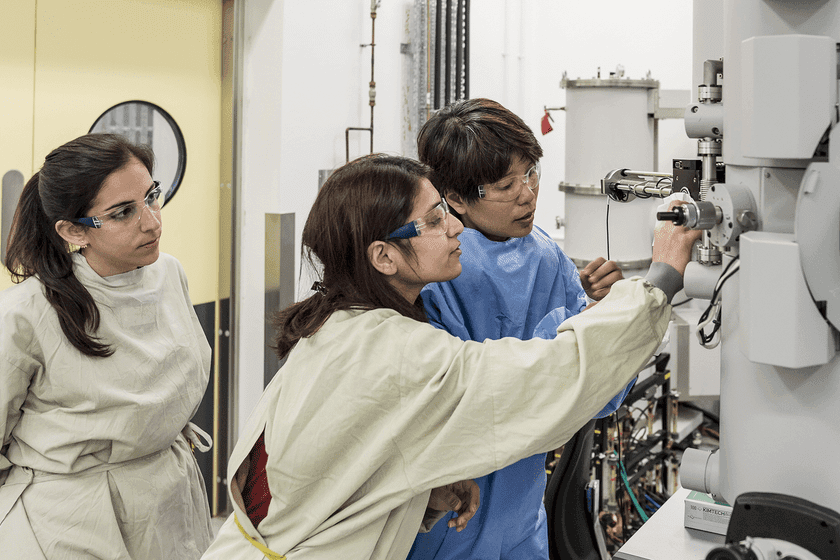 Three female researchers look at machinery in a lab.