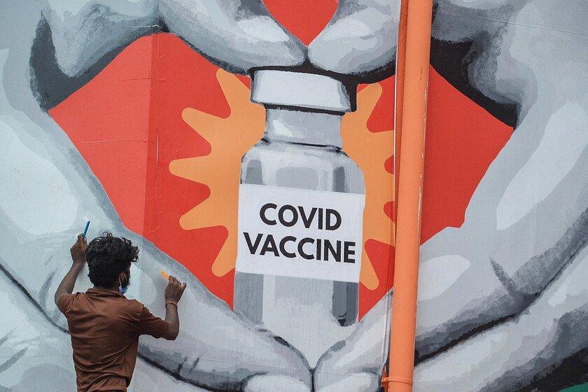 A man gives finishing touches to a huge mural that shows a Covid vaccine vile inside a heart hand. 
