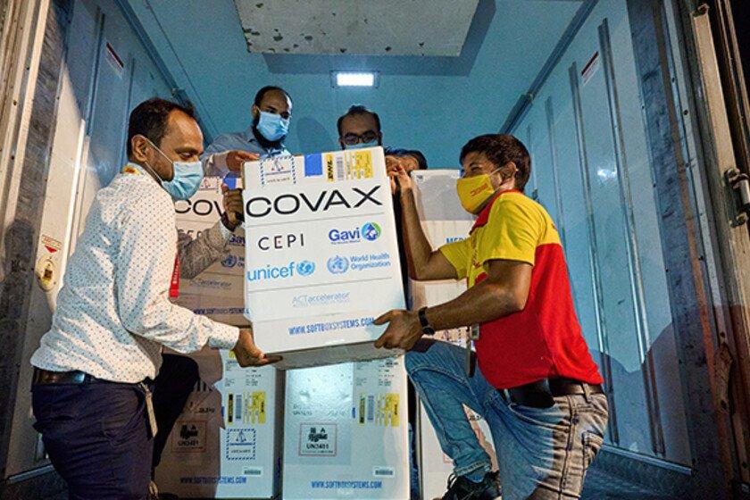A group of men unload a box that says 'COVAX' from a truck.