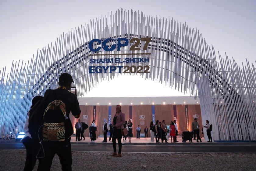 A large metal archway with a sign that reads 'COP27 Sharm El Skeikh Egypt 2022' on it, leading to a conference centre