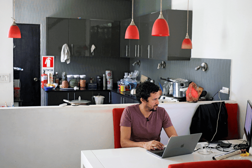 Male researcher sits at desk in his kitchen and looks at laptop