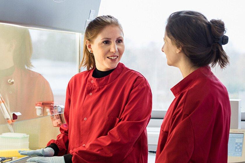 Two women wearing red lab coats talking to each other