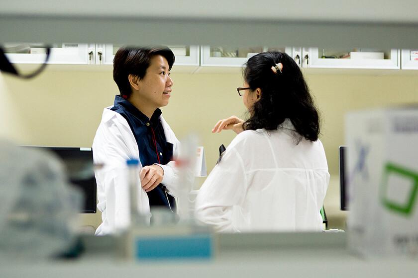 Two women wearing white lab coats talking to each other
