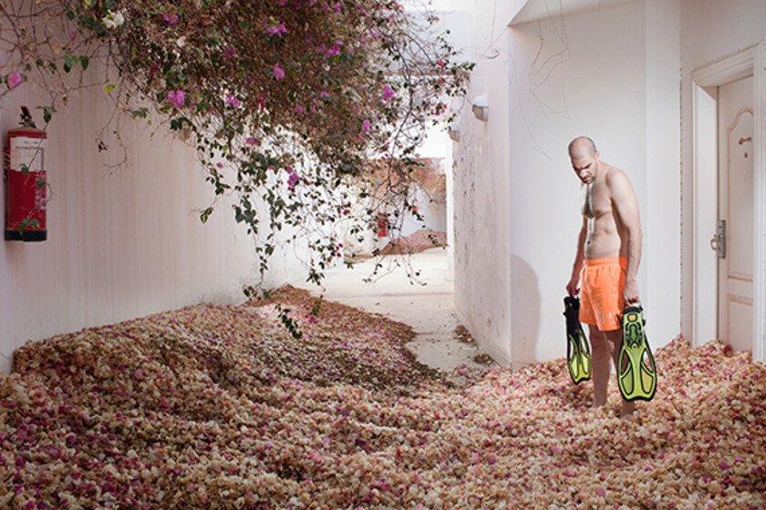 A man holding two flippers stands in a hotel room overgrown with rose bushes