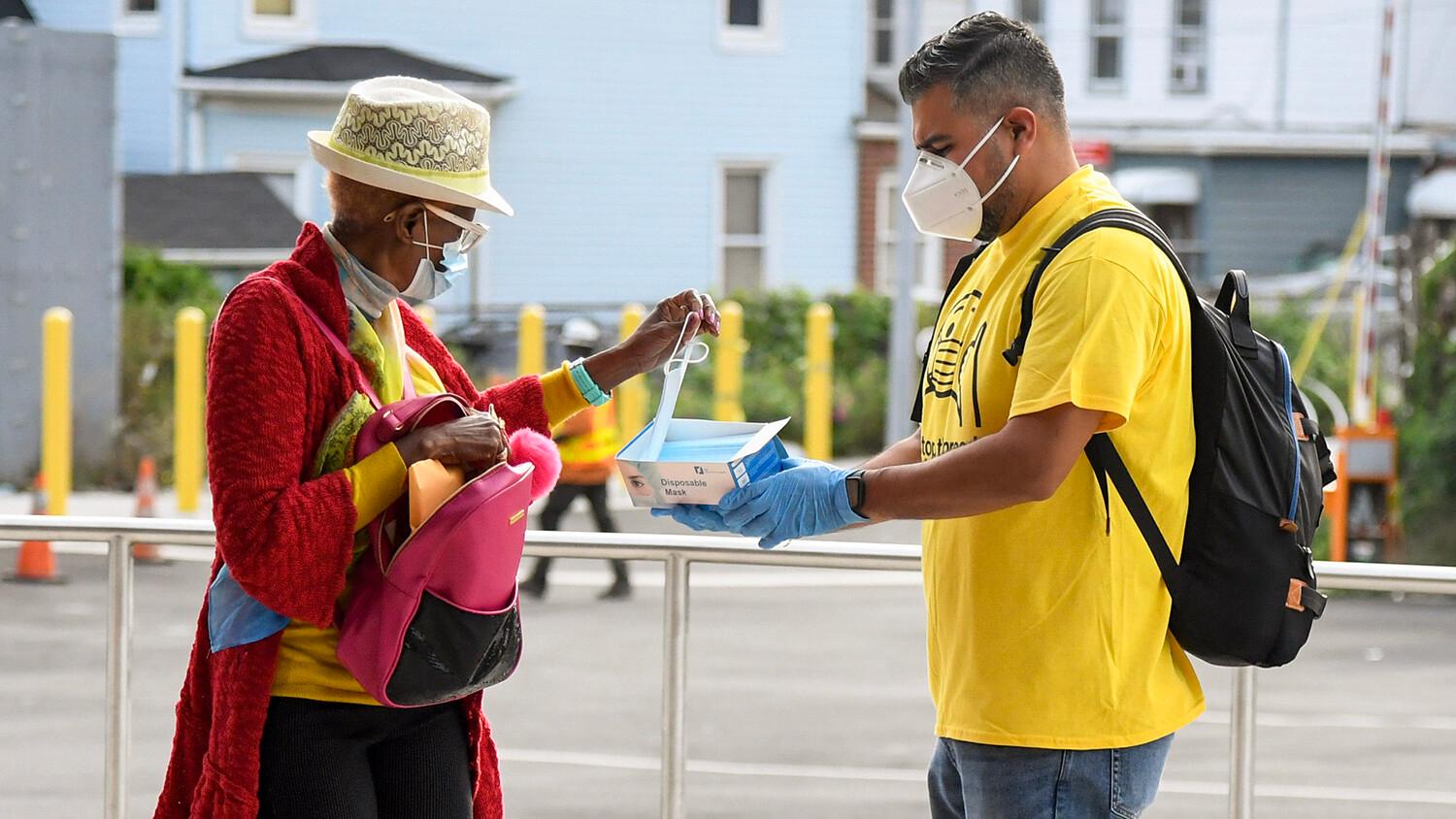 A volunteer offers a passer-by a face mask.