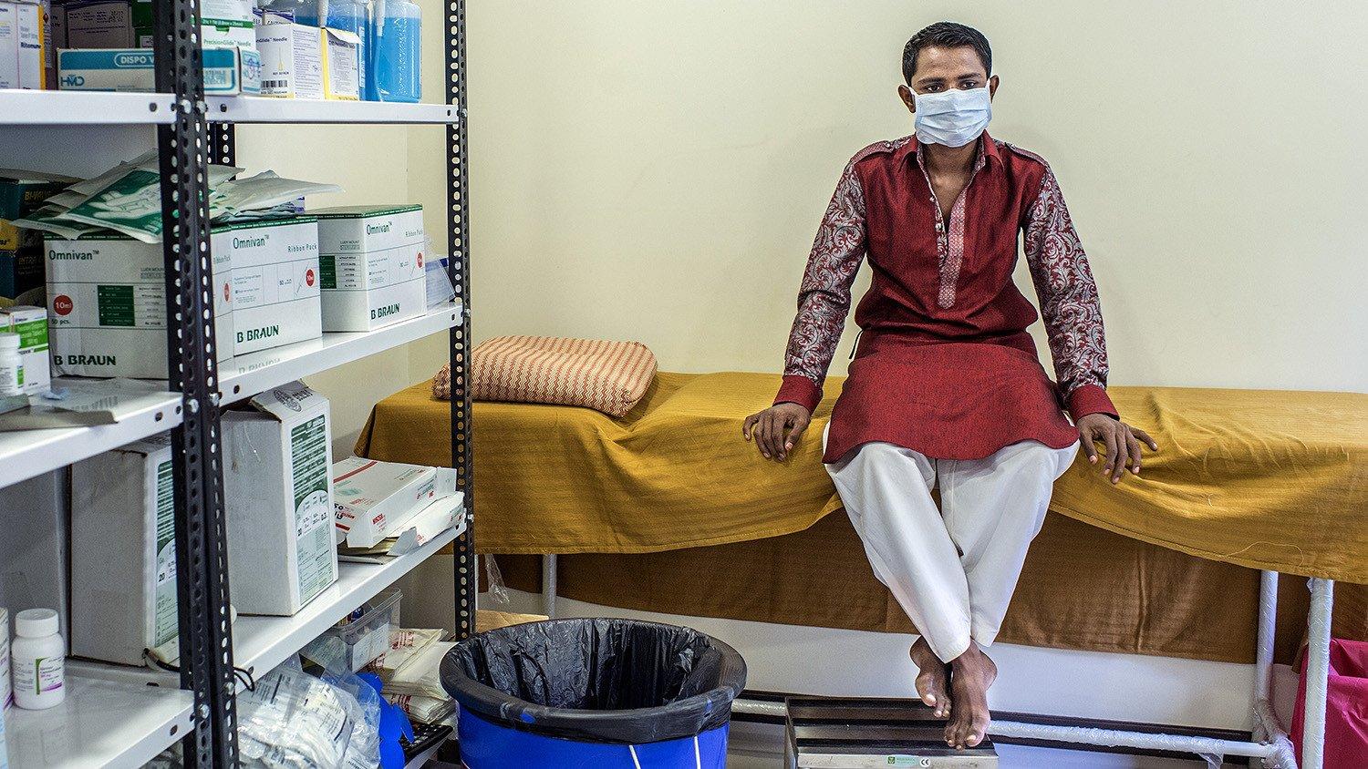 Patient wearing a face mask sits on a bed in a clinic
