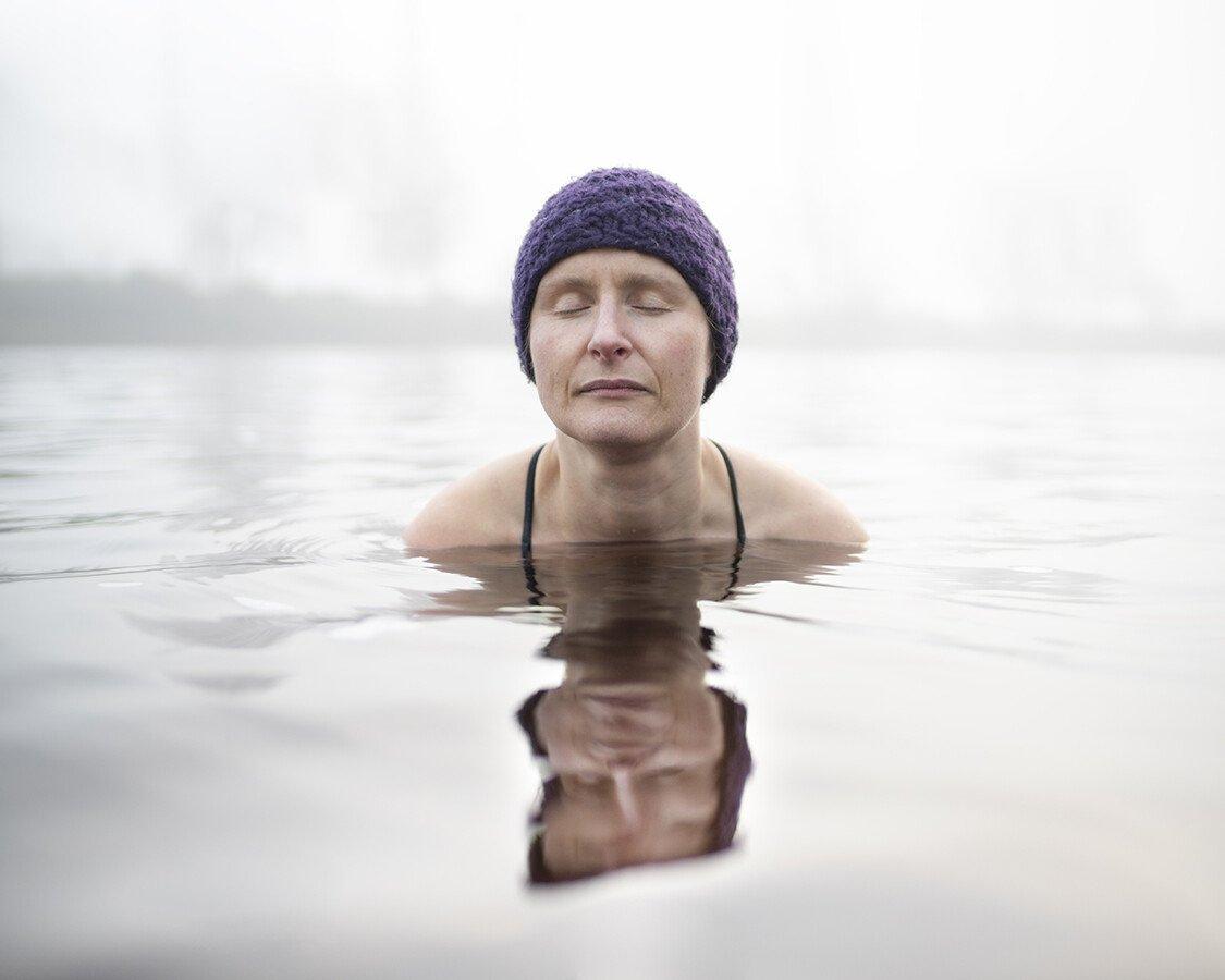 A woman wearing a swimming cap swims in cold water with her eyes closed