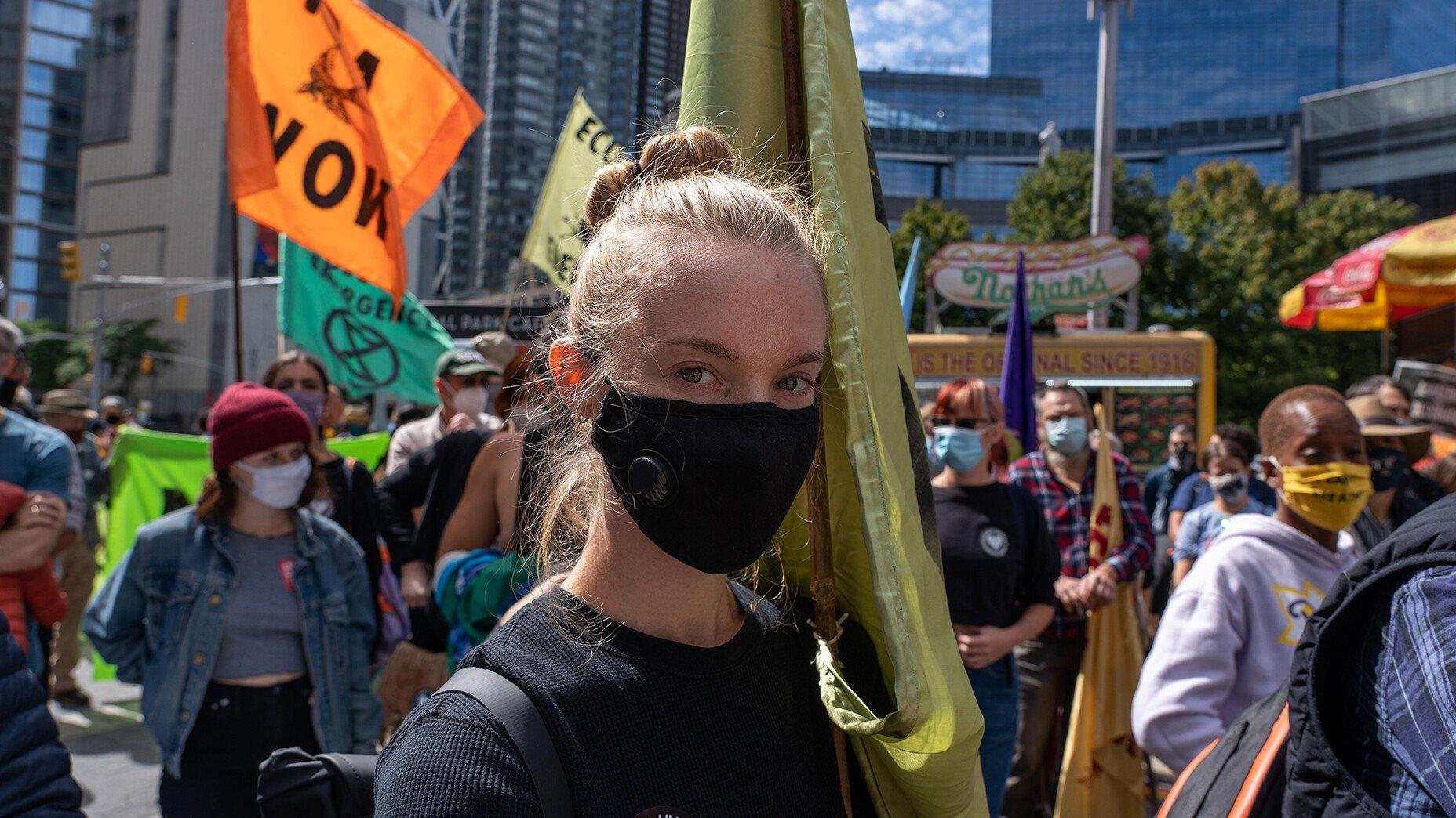A young girl wearing a mask holds a flag during a climate march.