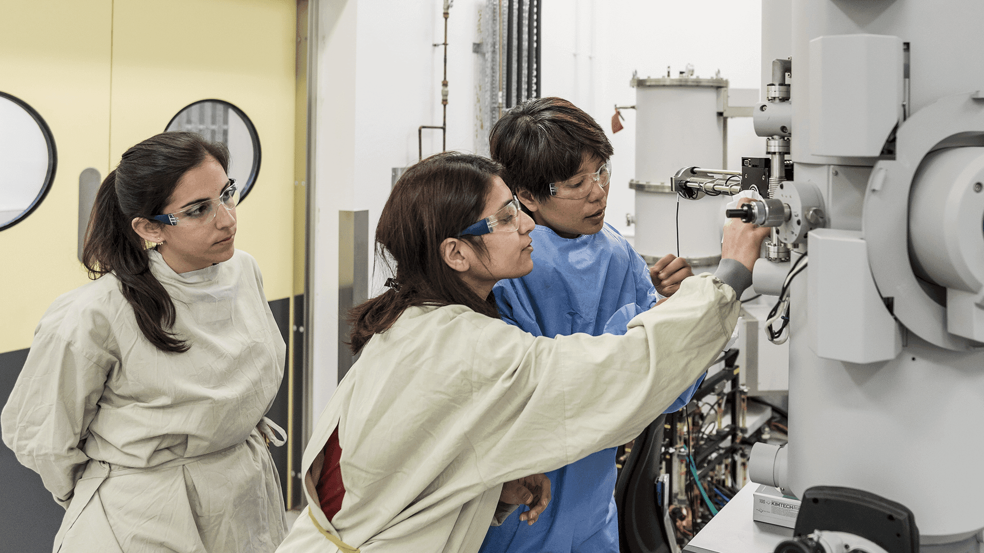 Three female researchers look at machinery in a lab.