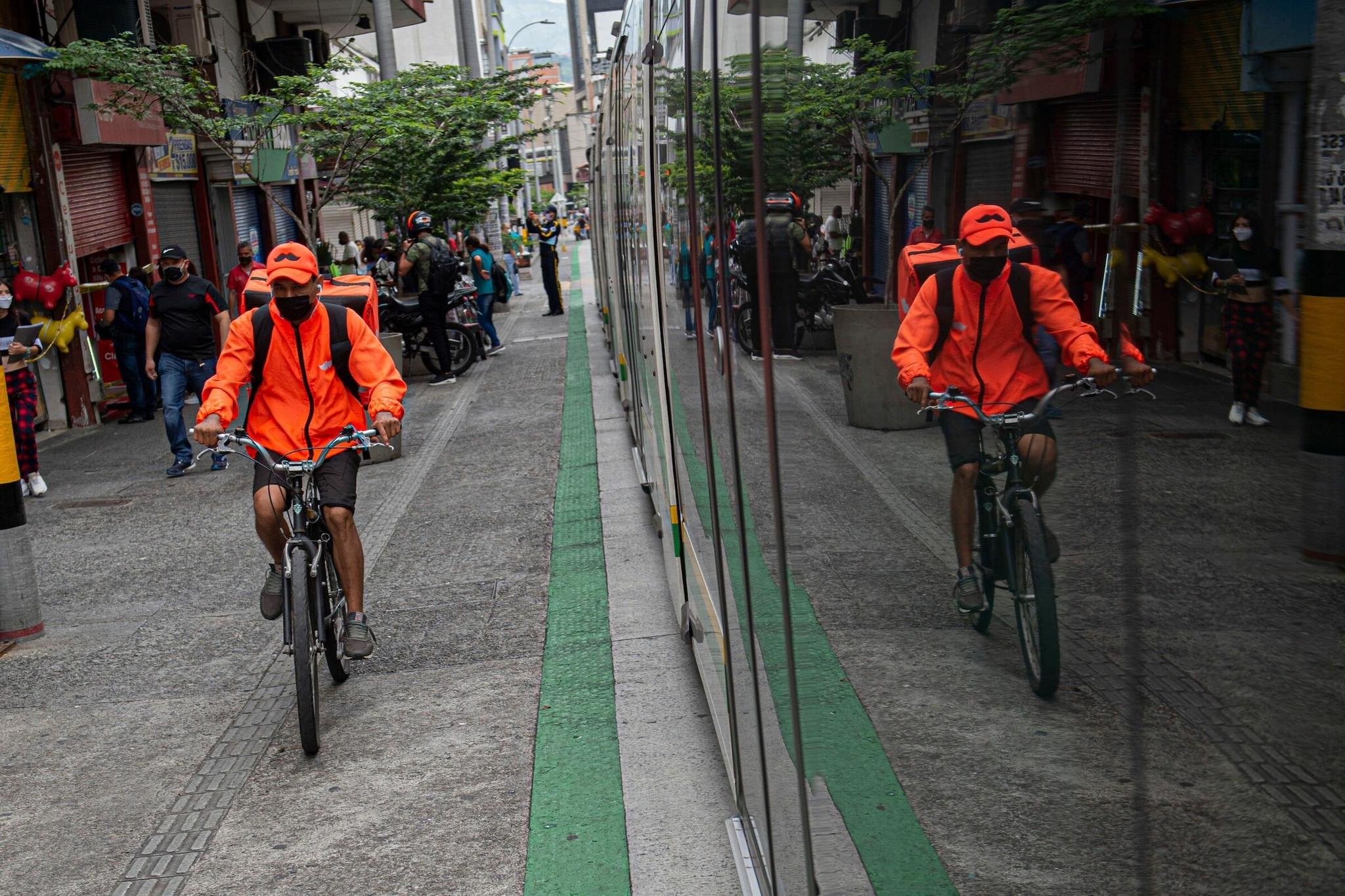 A man rides a delivery bicycle next to the tram amid the COVID-19 pandemic, in Medellin, Colombia.