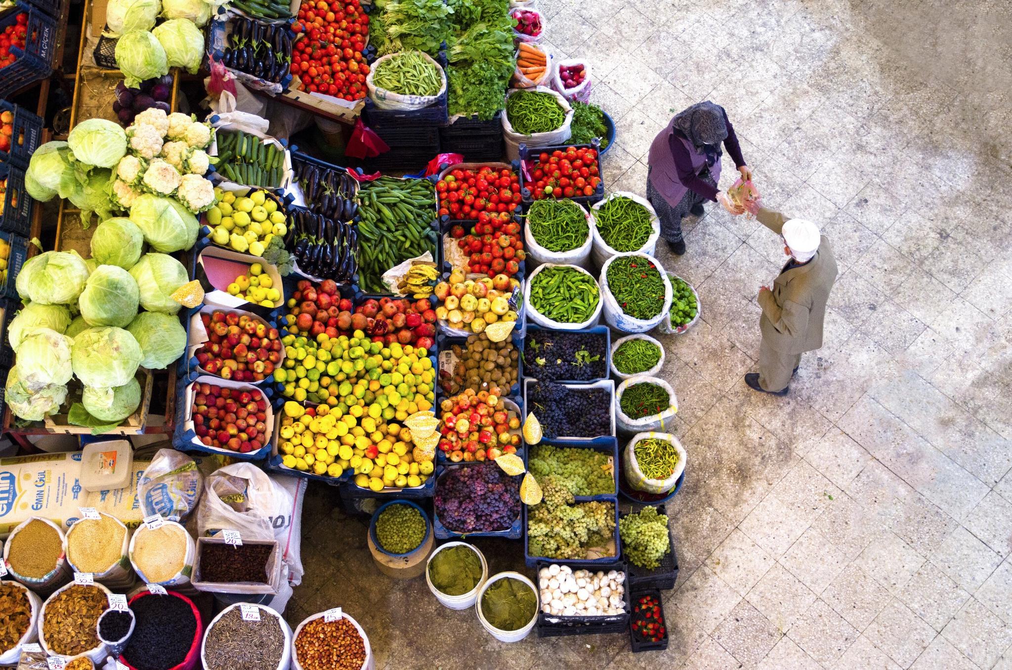Top view of a woman and man next to colourful vegetables and fruits stands.