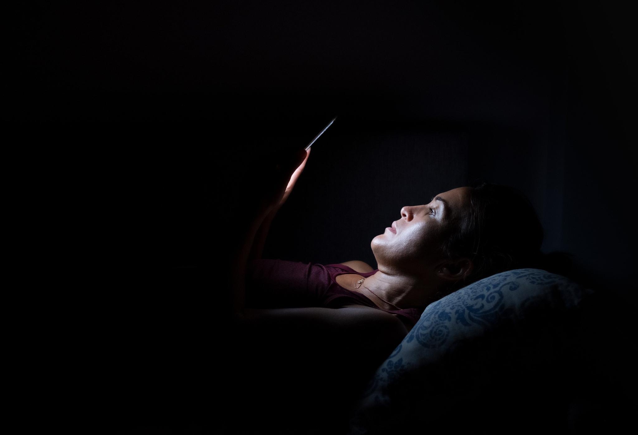 Young woman lying in the dark looking at her phone.