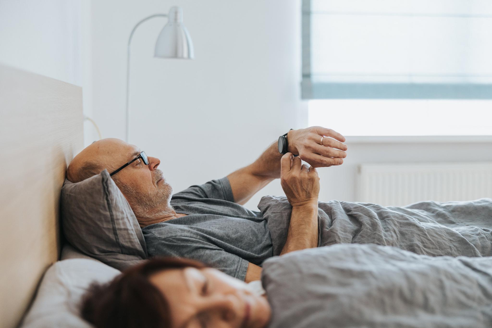 A man looks at a smartwatch in bed.