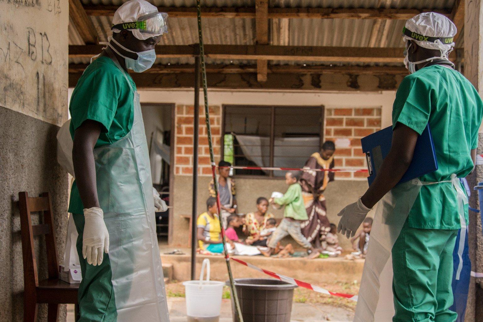 Two medical staff outside of a monkeypox quarantine area in the Central African Republic with children visible in the background