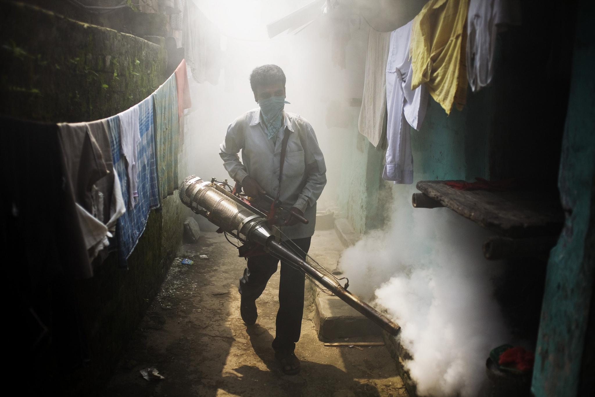 A man holds a contraption that sprays fog to kill mosquitoes in a neighbourhood of houses.