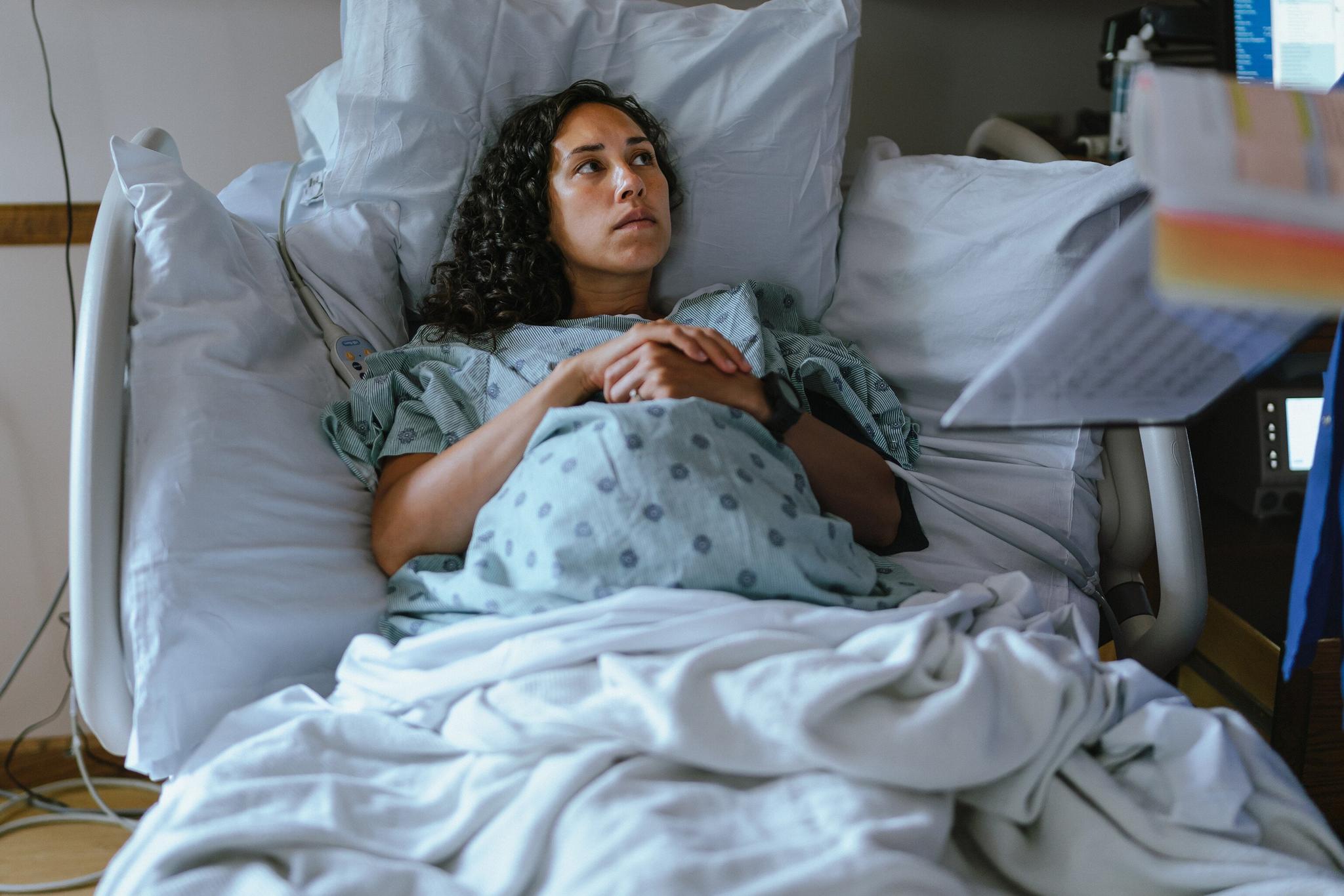 A pregnant woman in a hospital bed speaking with a doctor.