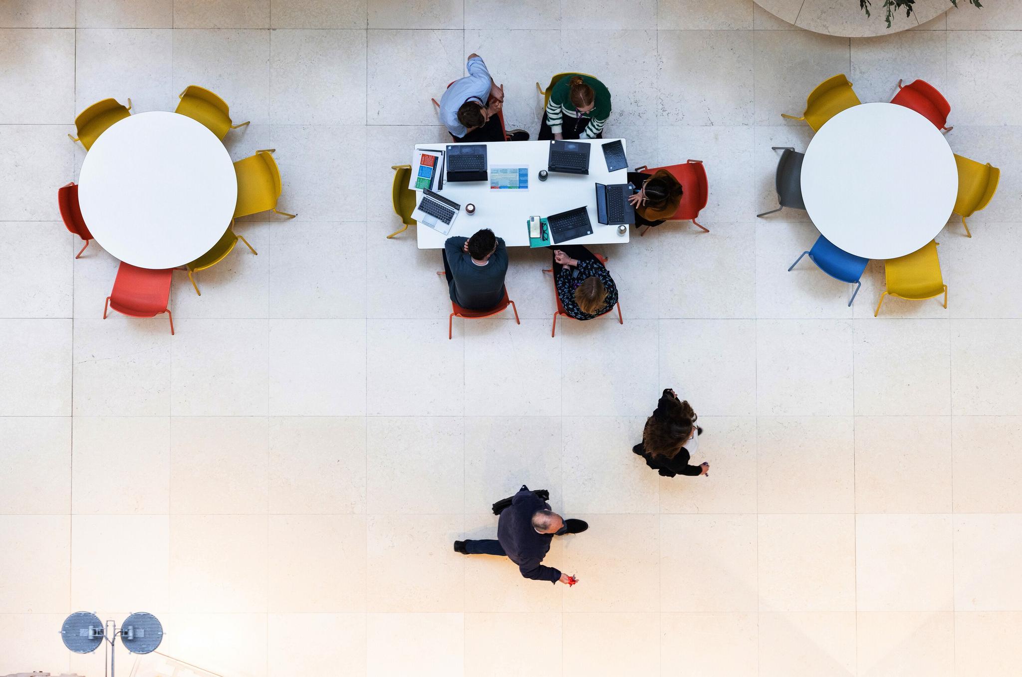 Round tables in an office environment with people working on them, seen from above