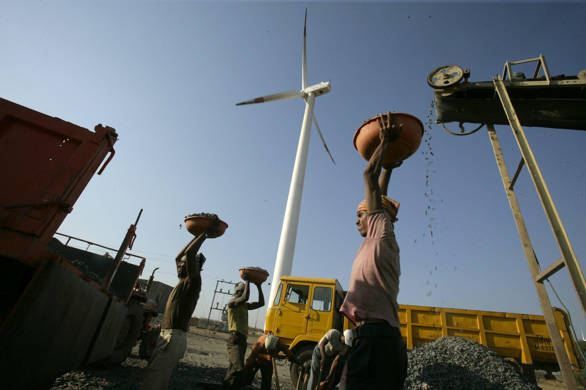 A photograph of a man carrying fuel with a wind turbine in the background