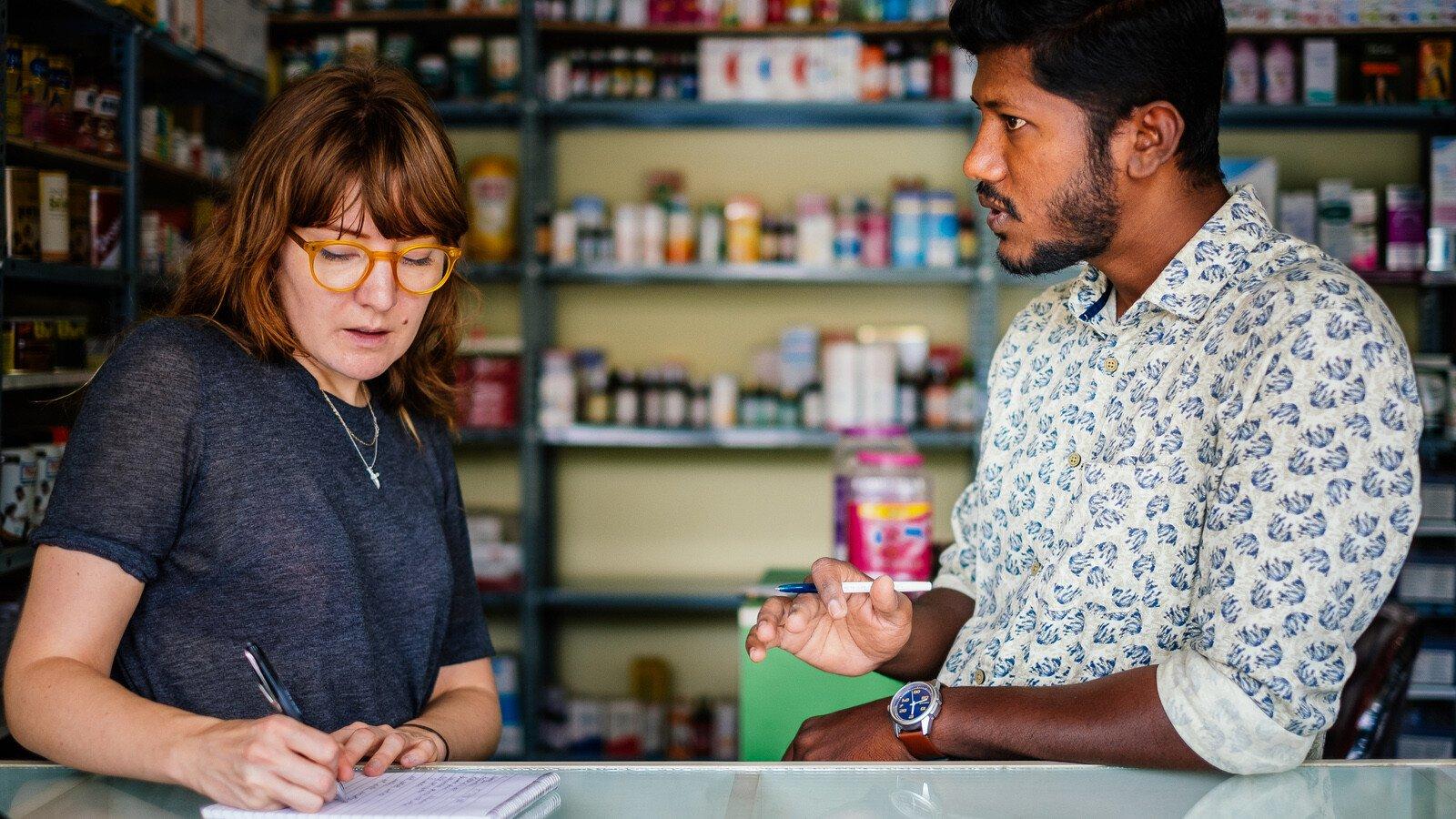 A pharmacist talking and a researcher taking notes in a pharmacy in Bangalore, India.