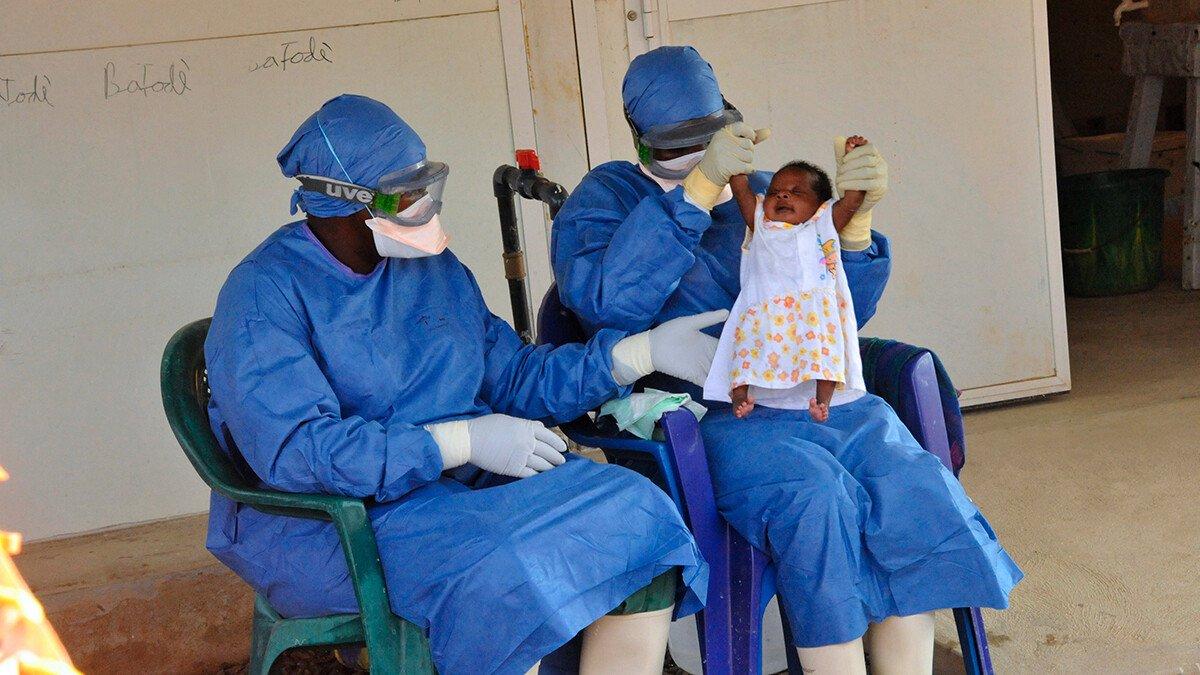 Two medical workers hold up baby Noubia, the last known patient to contract Ebola in Guinea