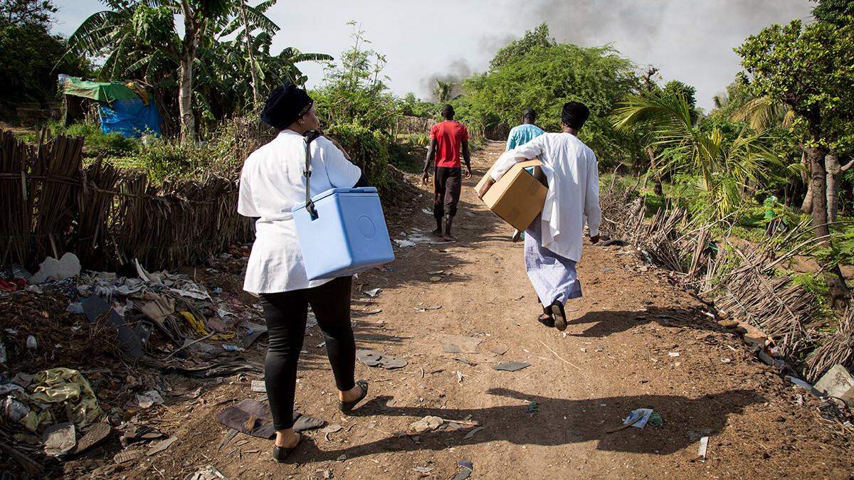 Four health workers carry portable vaccine cold storage boxes